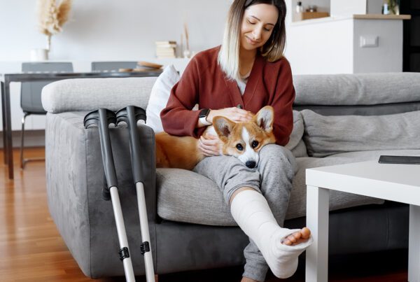 Employee Benefits - Woman With Crutches Sitting Down on a Sofa Petting Her Dog at Home