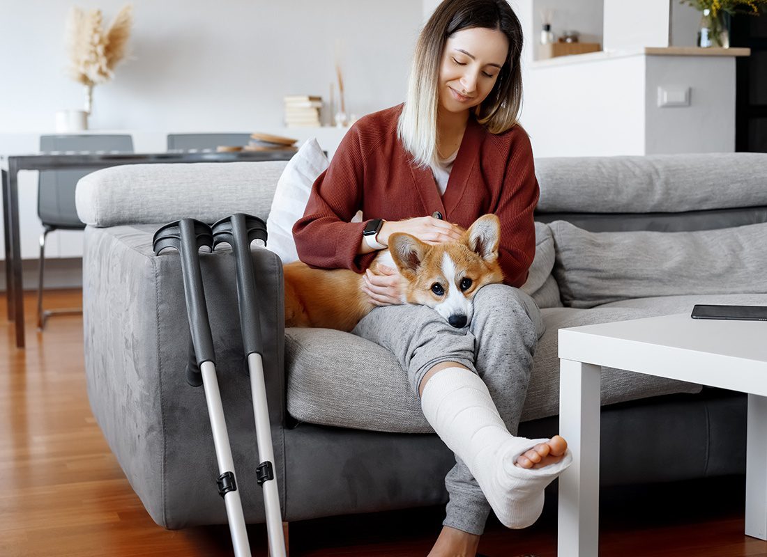 Employee Benefits - Woman With Crutches Sitting Down on a Sofa Petting Her Dog at Home