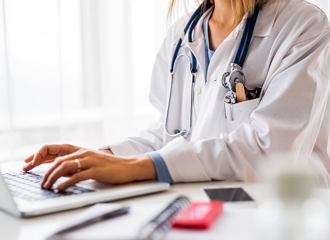 Medicare FAQ - Close-up of Female Doctor Typing on a Laptop