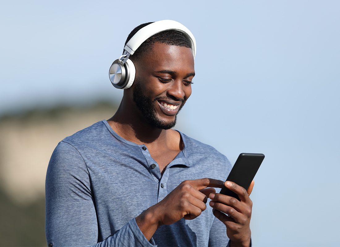 Video Library - Man Smiling with Headphones On While Walking Outside and Watching a Video on His Phone